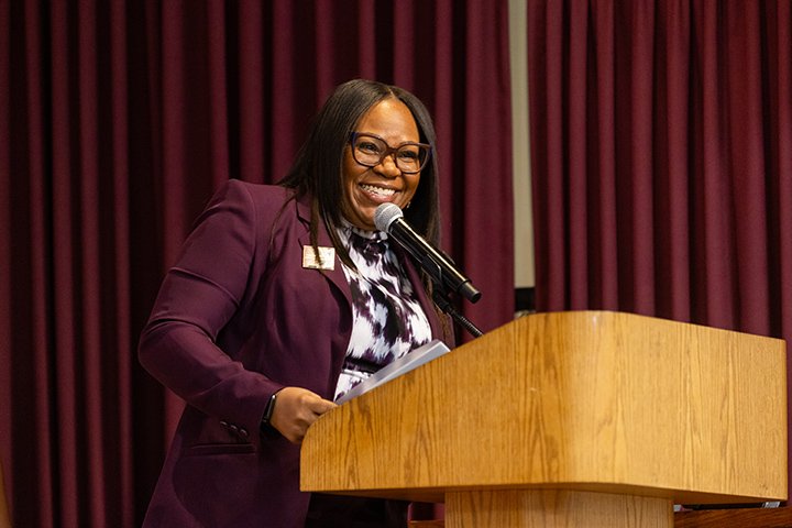 A woman wearing a maroon blazer stands at a podium in front of a maroon curtain during the annual Black Girls Rock Awards Show.