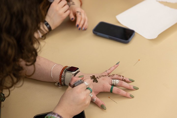 A person applies henna to their hand while resting it on a table.