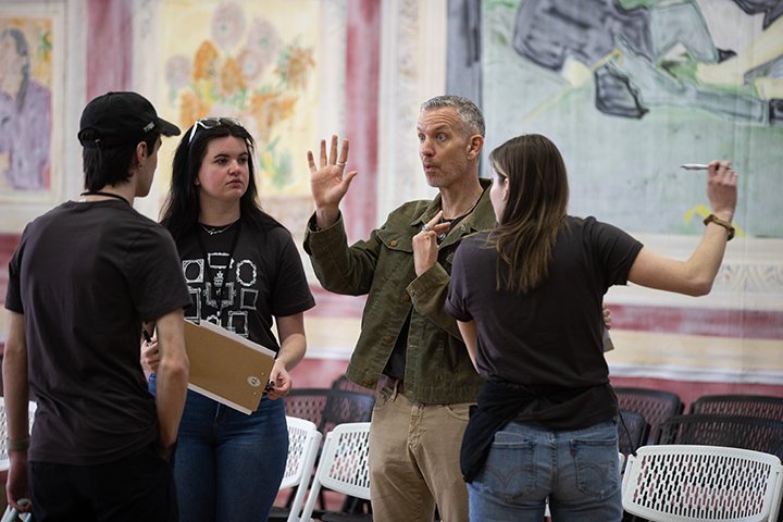 Faculty member Ian Mull speaks with a group of three students in a classroom.