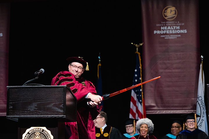 At CMU spring commencement, President Davies stands on stage swinging a light saber.