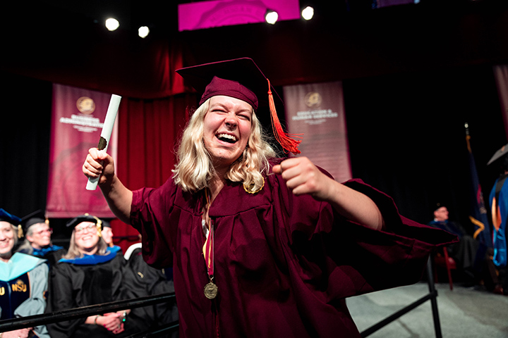 At CMU spring commencement, a graduate with blonde hair smiles while holding her diploma in one hand.