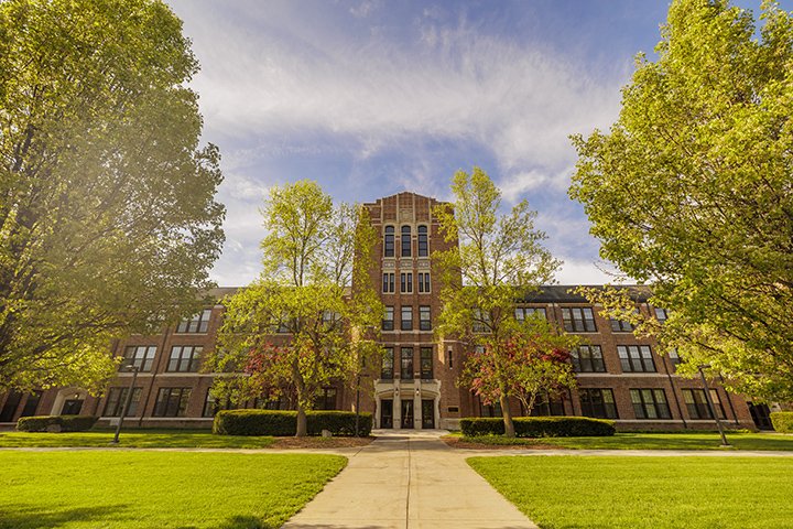 On a sunny day, Warriner Hall stands tall against a blue sky surrounded by green trees.