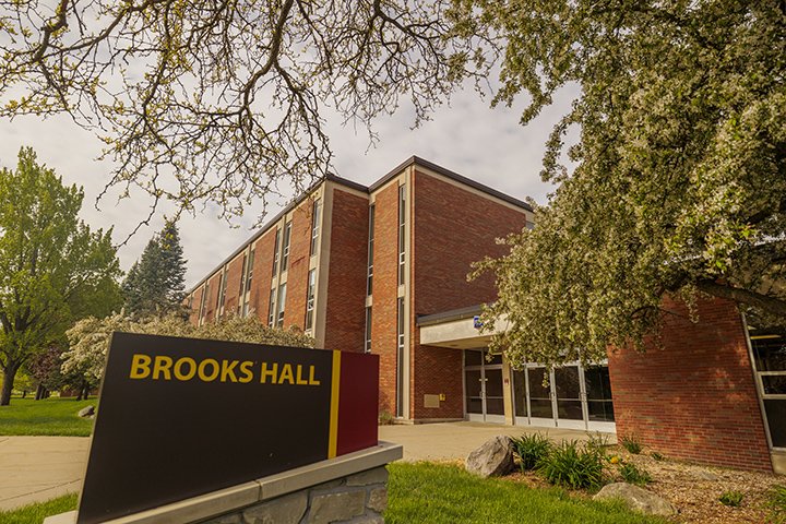 A lower-angle view of Brooks Hall with a Brooks Hall sign in front of it.