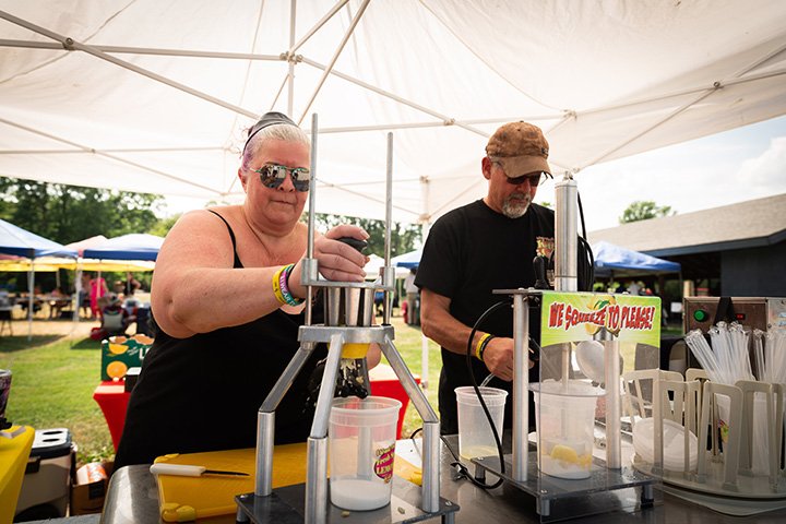 A middle-aged man and woman squeeze lemons using a juicer to make lemonade.