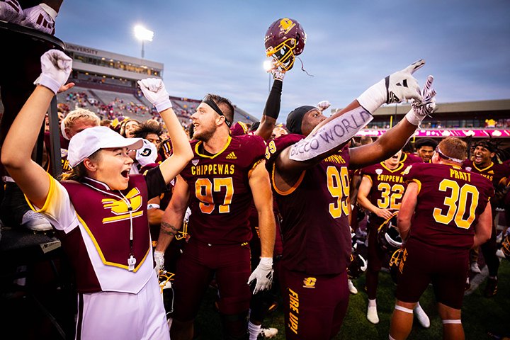 CMU football players and band members raise their arms in celebration after a win.