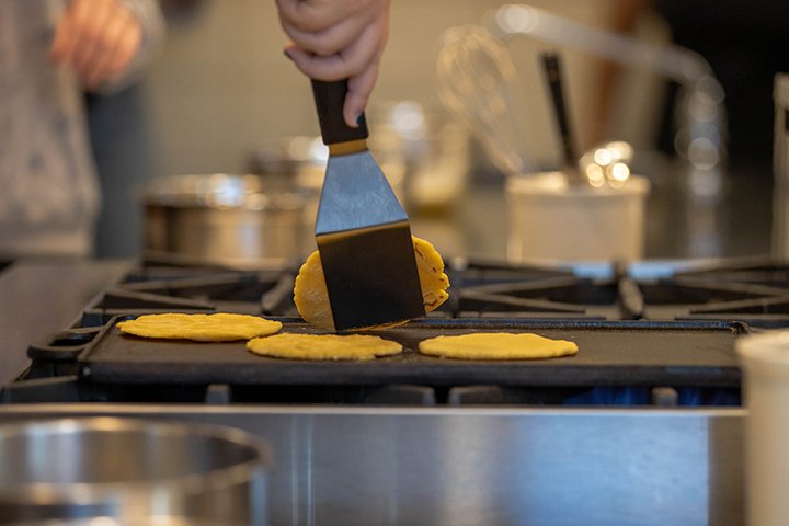 A closeup of a spatula scooping tortillas off a stovetop.