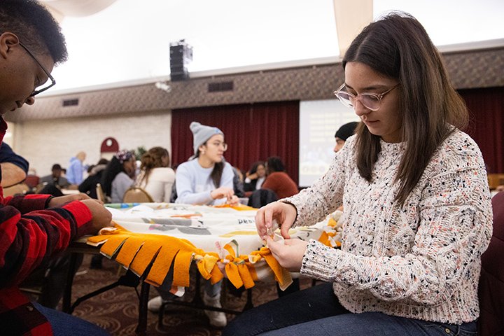 Students sit at a table turning sheets of fleece into blankets.