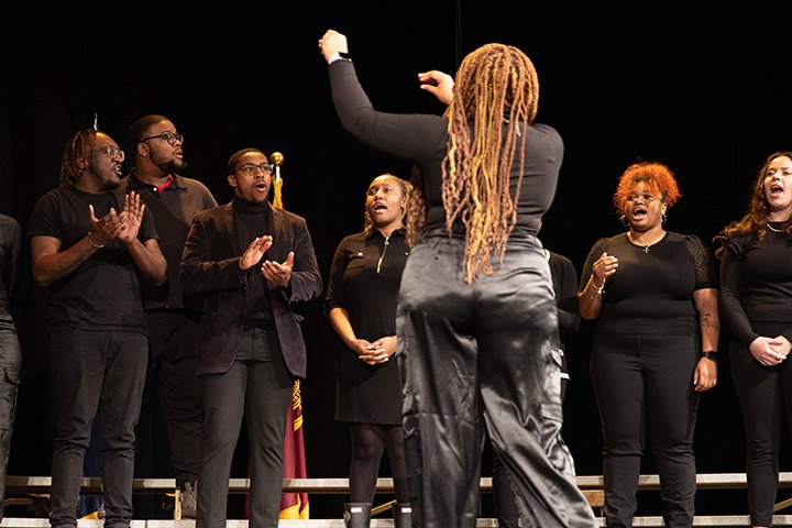 The Christ Central Choir performs on the stage inside Plachta Auditorium while the choice director stands in front of the group with her back to the crowd.
