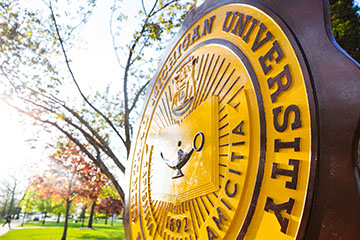 Maroon and gold CMU seal seen from an angle as spring sunshine reflects off its face.