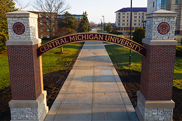 The Central Michigan University Voisin Arch stands over a campus sidewalk in the early morning spring sunlight.