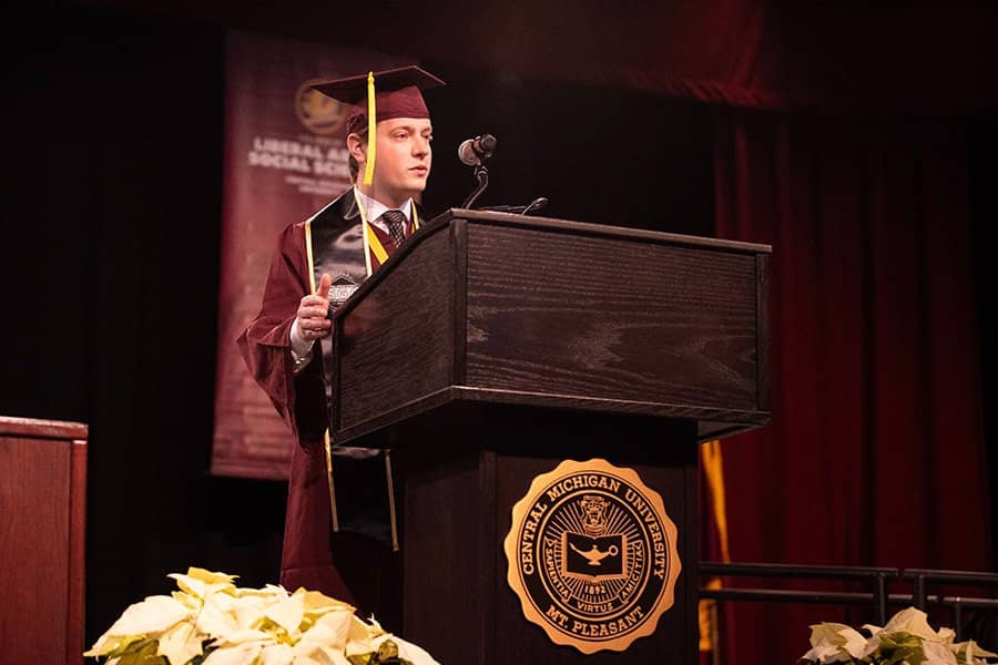 A man in a graduation cap and gown standing at a podium.