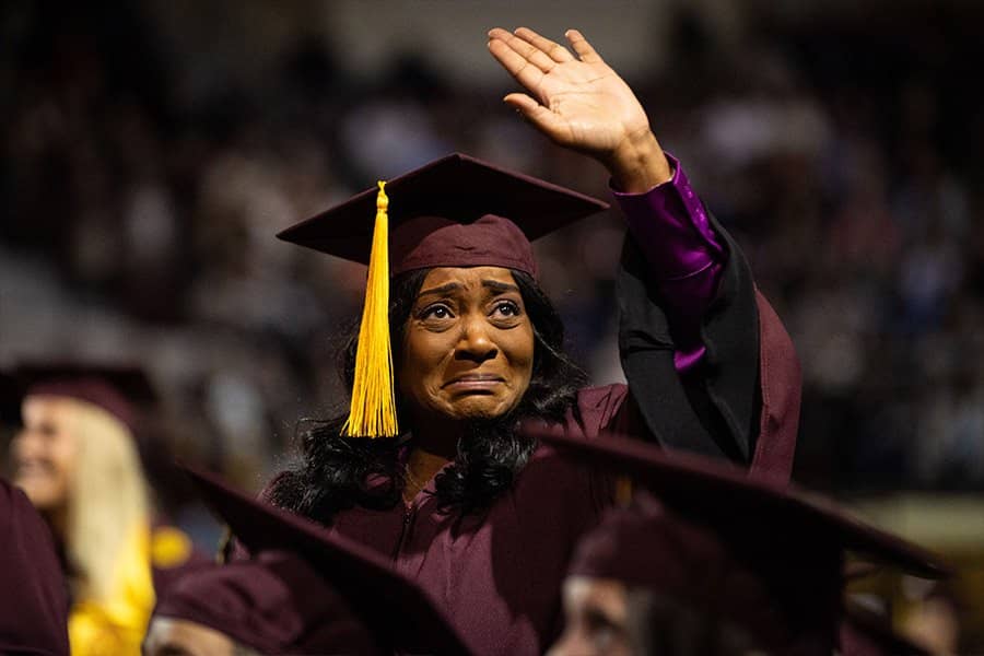 a woman in a graduation cap and gown waving at family members
