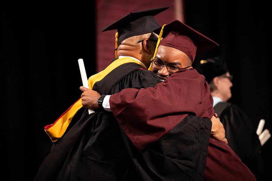 Two men in graduation gowns hugging