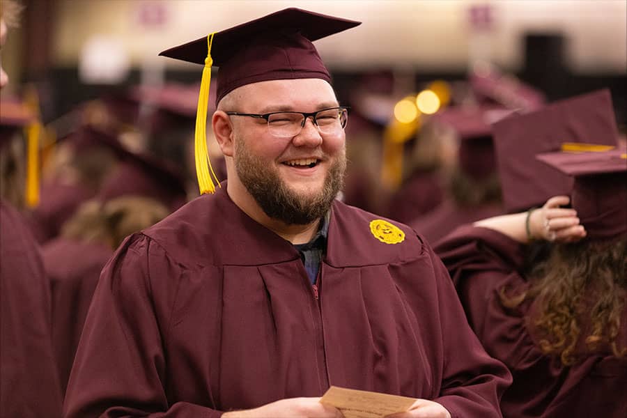 A bearded man in a graduation gown smiling.