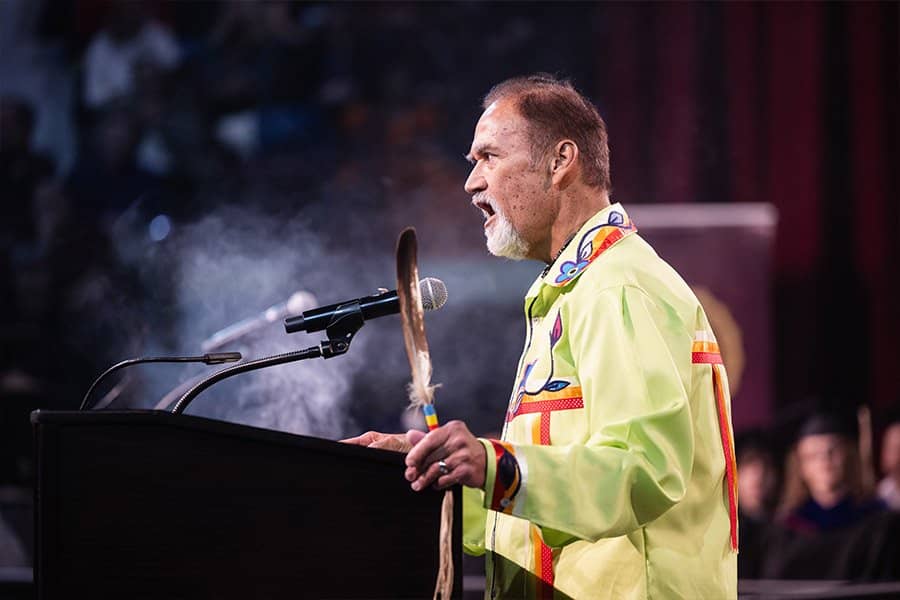 A man in a yellow shirt standing at a podium with a feather in his hand.