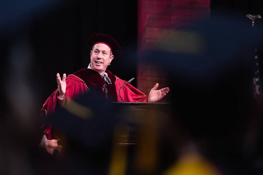 a man in a maroon graduation gown speaking at a podium