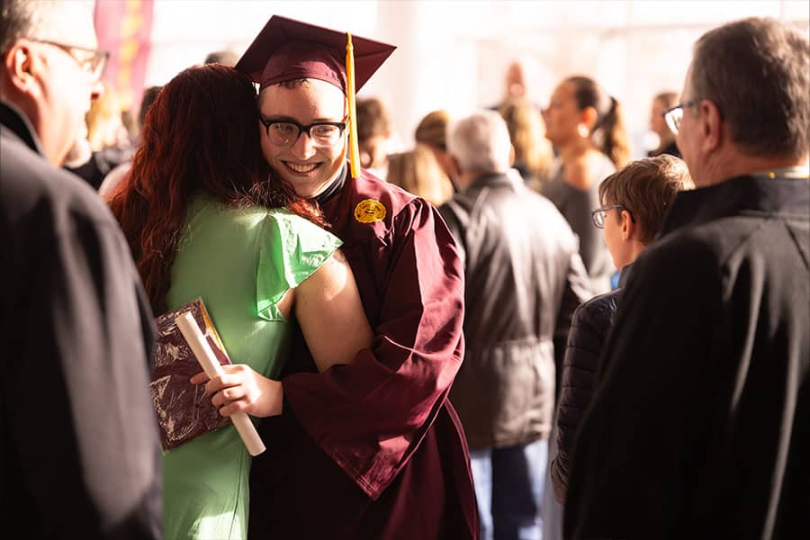a man in a cap and gown hugging a woman in a crowd