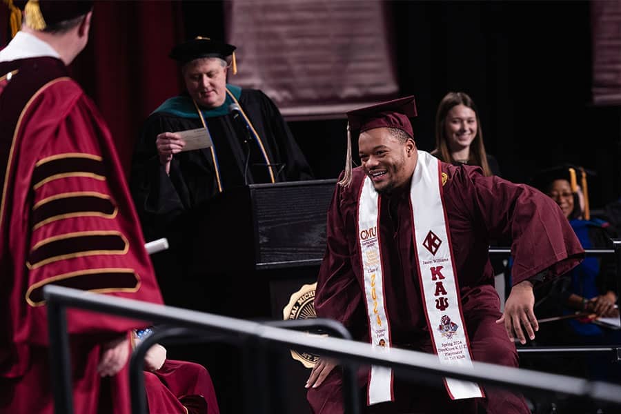 a man in a maroon graduation cap and gown dancing onto a stage