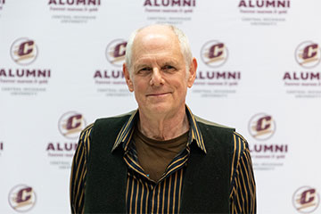 Close-up photo of a smiling man wearing a gold shirt and black vest