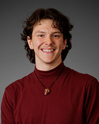 The head and shoulders of a smiling young man wearing a maroon turtleneck sweater.