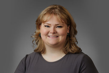 A blonde woman wearing a grey shirt smiles at the camera.