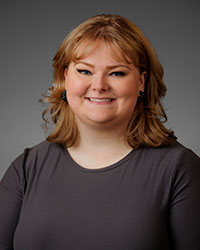 A blond woman in a grey shirt smiles at the camera.