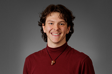A smiling young man wearing a maroon turtleneck shirt.