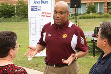 A man wearing a maroon CMU polo shirt stands and talks to two women outside the CMU library.