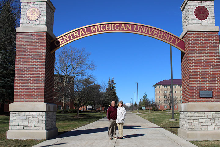 A man and woman stand together beneath an archway that reads Central Michigan University