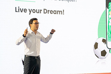 A man in a white dress shirt and slacks stands with arms half-outstretched under the words, "Live your Dream" with a soccer ball on the right edge of the image.