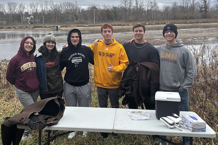 Six young people stand behind an outdoor table with sampling equipment on it.