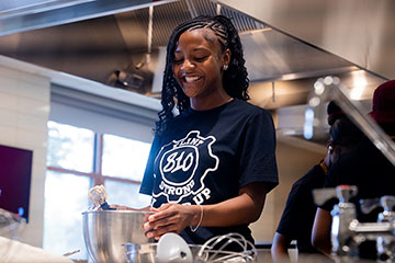 A smiling young woman looks down at a mixing bowl.