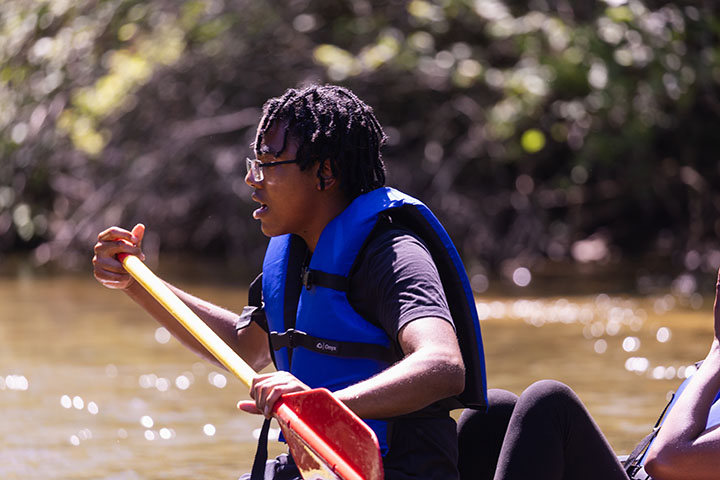 A young man wearing a blue life jacket and holding a canoe paddle looks intently ahead of him.
