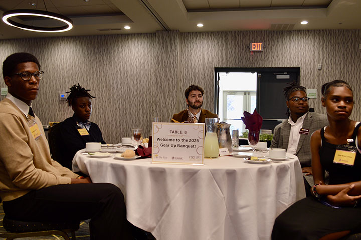 Five young people in business casual clothing watch a presentation unfold off screen.