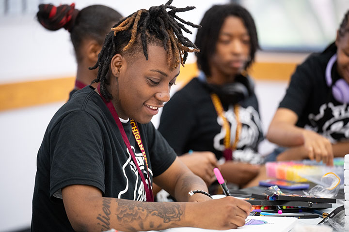 A smiling young man colors a picture on a piece of paper.