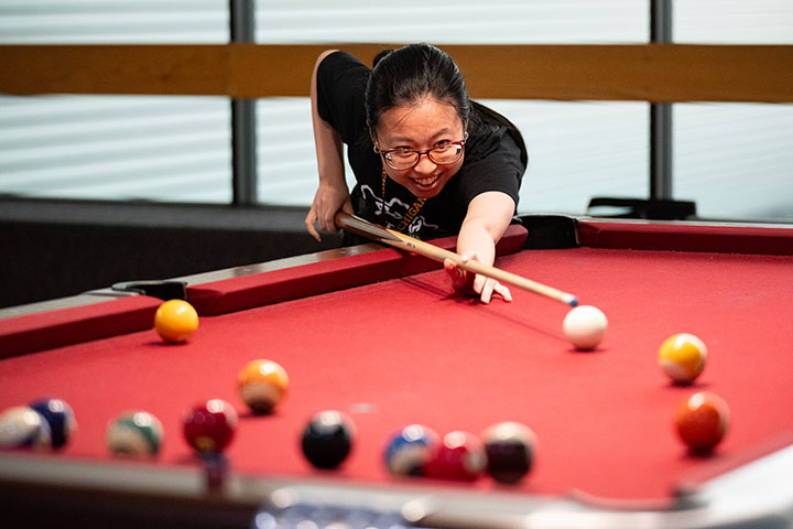 A smiling young woman bent over a pool table lines up a shot.