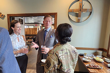 A man in a suit talks to a woman in an army uniform while a second woman looks on while holding a glass.
