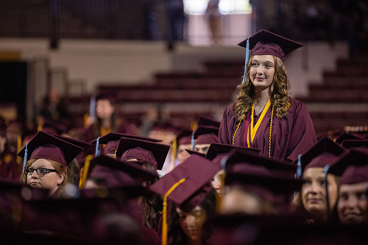 A woman in a maroon graduation gown standing among a group of people.
