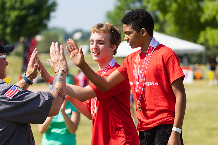 Two Special Olympic Michigan athletes high five a law enforcement officer after receiving award medals.