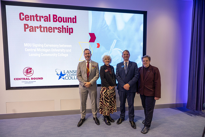Four people, including CMU's president and provost, stand in front of a large projector screen with the words Central Bound Partnership on it
