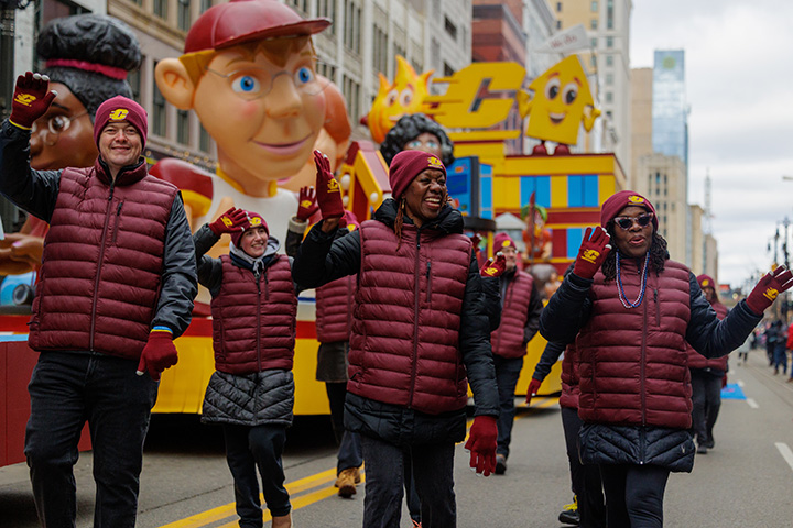 CMU parade walkers, wearing maroon vests and CMU hats and gloves, wave to the crowd
