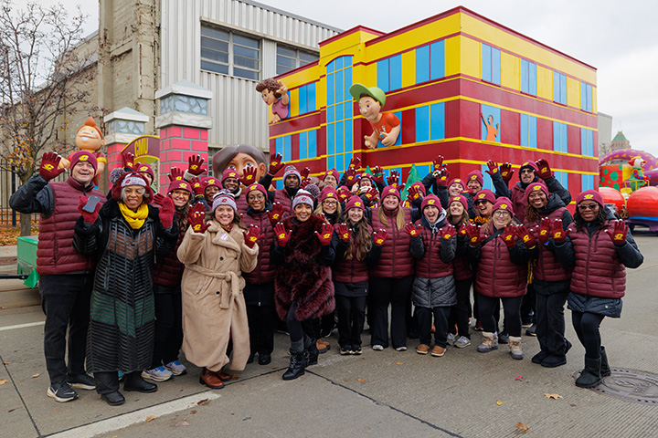 A large group of people dressed in CMU clothing pose for a photo in front of the CMU Thanksgiving parade float