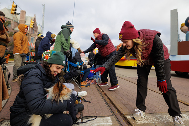 CMU parade walkers greet spectators, including a woman sitting on the ground holding a collie dog
