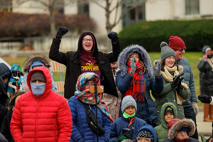 Excited parade watchers, including one wearing a a CMU Chippewas sweatshirt, cheer and clap