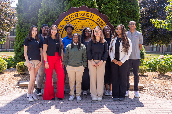 A group of students posing for a photo in front of the CMU seal.