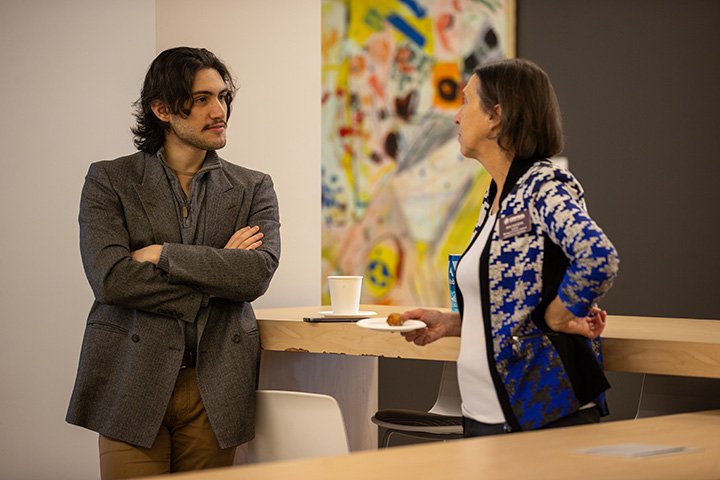 Two people lean against a table and talk to each other.