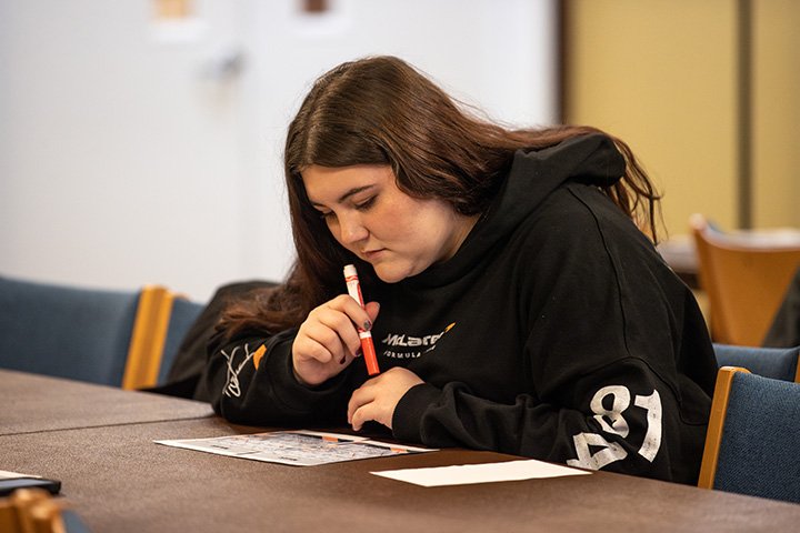 A female student sits at a table, holding a marker and playing BINGO.