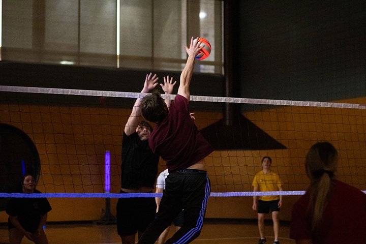 College students play volleyball indoors.