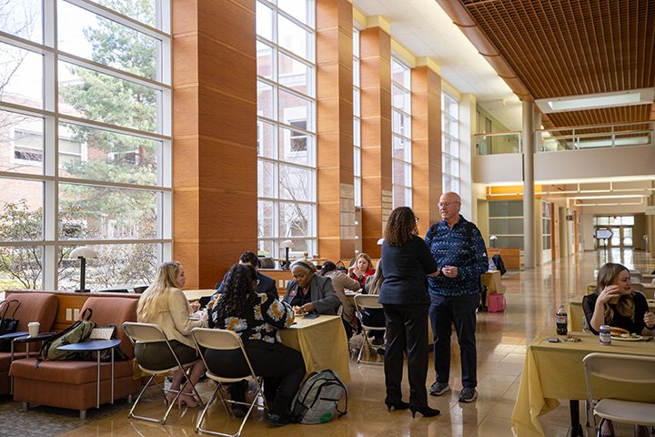 Student and faculty stand in the well-lit atrium of the Health Professions building.