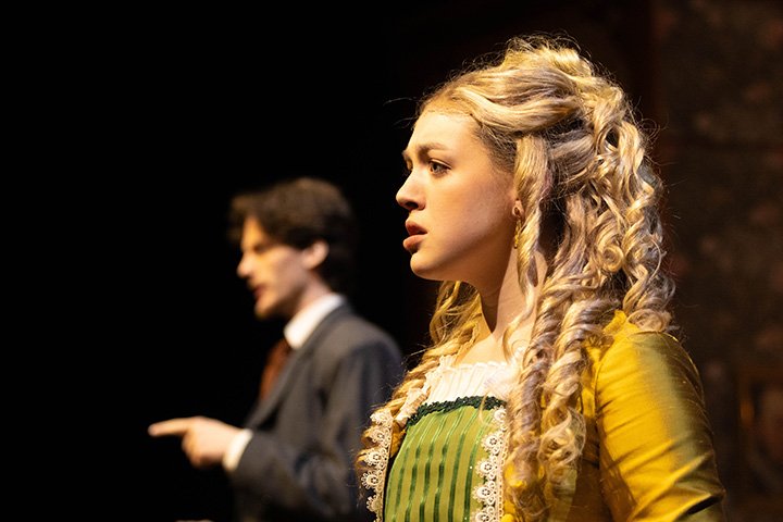 A blonde student actress in a yellow dress and curly hair.